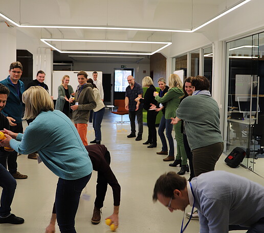 In a large room, workshop participants pass an orange ball to each other.