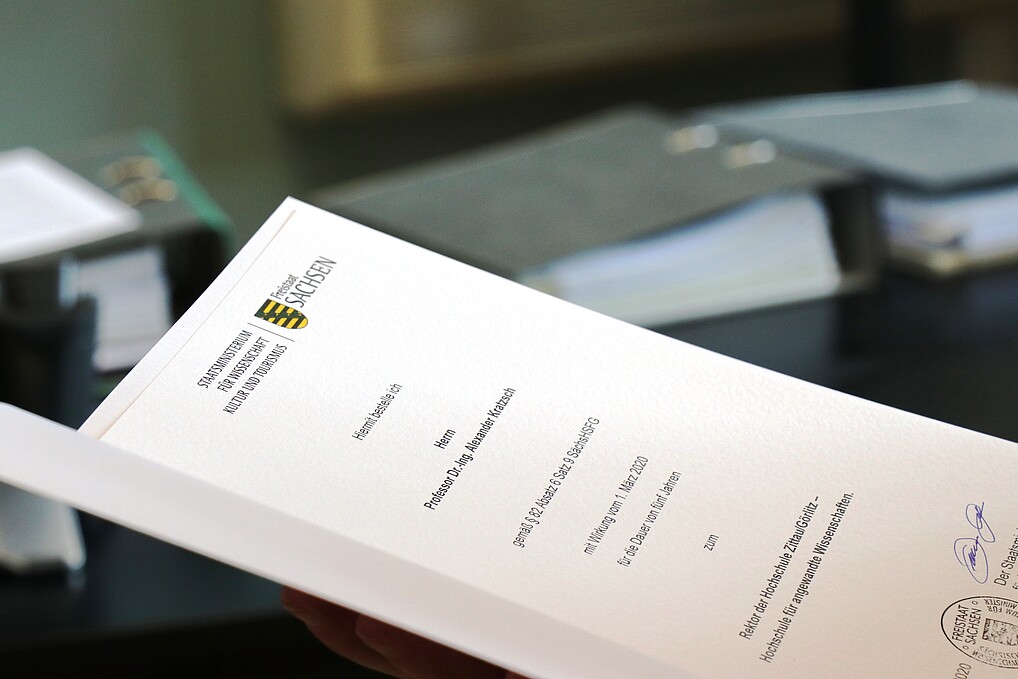 A close-up of a white document with many black letters, an important stamp and signature at the bottom. In the background you can see gray folders in the blur.