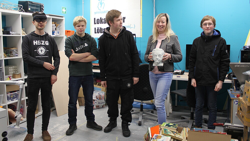 A group of pupils stand in the workroom with the smiling principal.