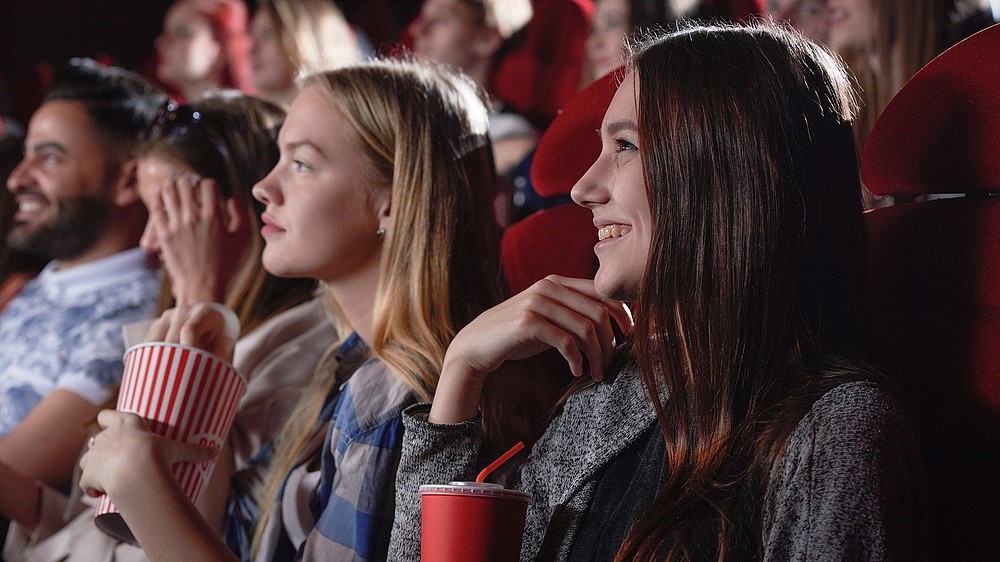 Mehrere junge Menschen sitzen im Kinosaal, Popcorn in der Hand und schauen lächelnd auf die Leinwand.