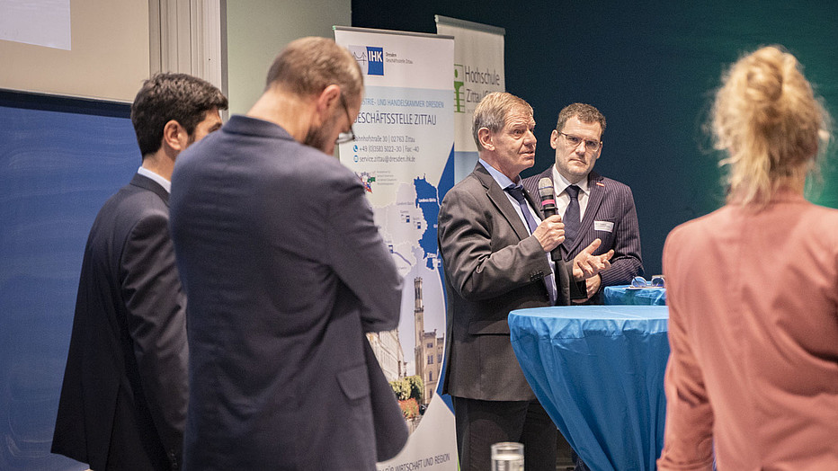Foto: Sven Müller Eine Gruppe von Veranstaltungsteilnehmenden steht im Veranstaltungssaal zusammen und hören einem Vortragenden zu.