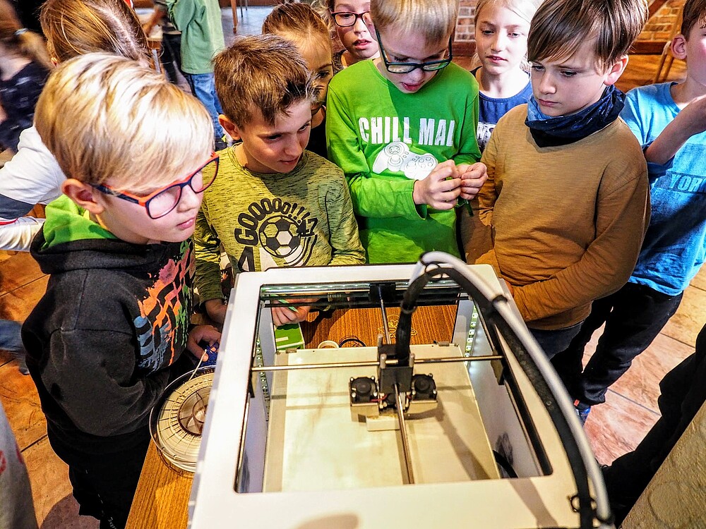 Kunder stehen vor dem 3D-Drucker und schauen ihm beim Druck zu