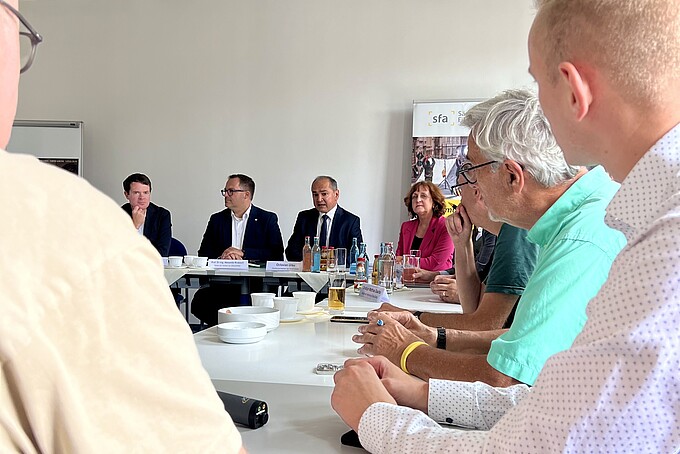 The shareholders sit at tables in a seminar room and discuss matters.