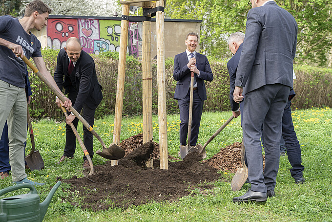 Gruppe von Personen nimmt aktiv an einer Baumpflanzzeremonie teil, arbeitet gemeinsam daran, ein Loch im Freien mit Erde zu füllen.