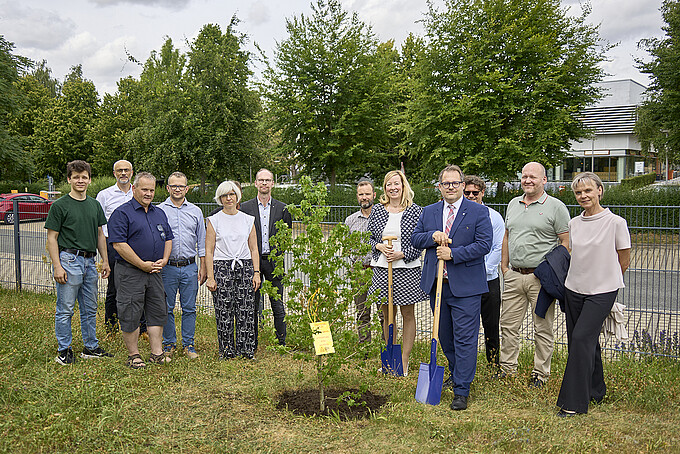 Some of the university management and university representatives are standing around a planted tree with shovels.