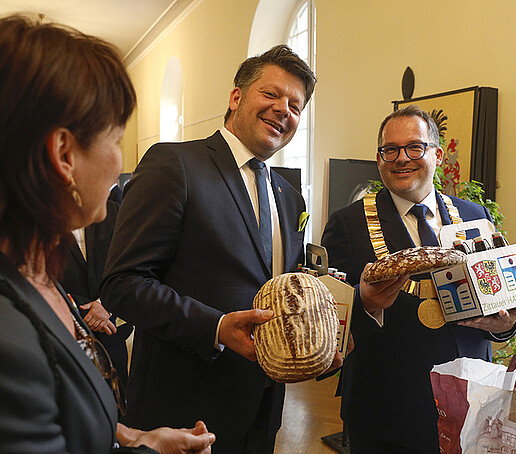 The principal accepts gifts from Mr. Zenker. There are two loaves of bread and a small crate of beer bottles. The box is labeled: Zittauer HAW-Bräu.