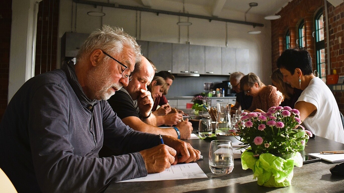 Workshop participants are sitting at a table at Celsiuz and taking written notes.