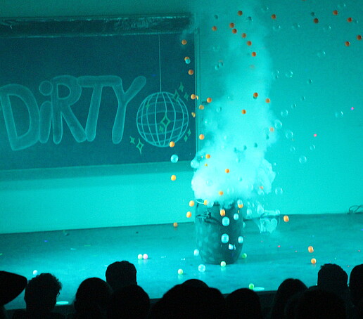 In the turquoise light, colorful balls fly out of a barrel on the stage.