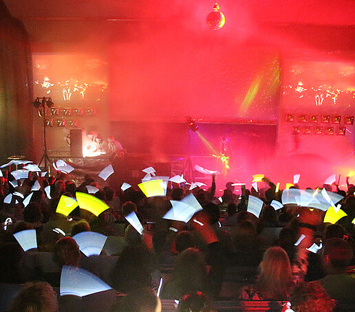 The audience waves with yellow glow sticks.