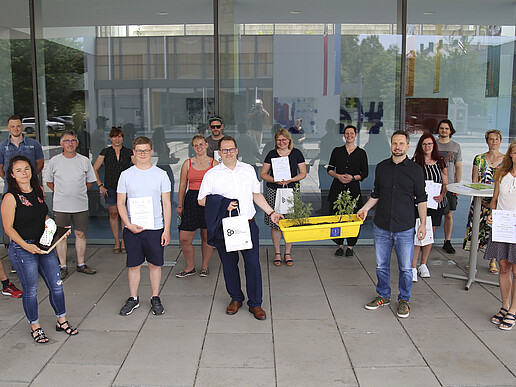 A large group of pedometer challenge participants stand in front of House 4 and smile at the camera. The winners hold their certificates up to the camera.
