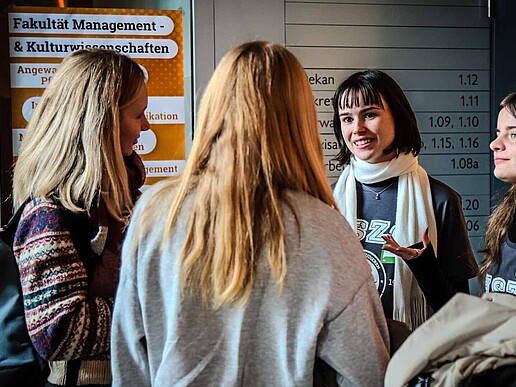 Four prospective students stand together as a group and talk in front of HSZG information boards.