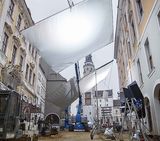 In einem Filmset in historischer Kulisse in Görlitz sieht man Filmschaffende und einen Leuchtschirm sowie weitere Filmtechnik.