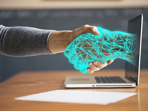 A hand shakes a digital hand sticking out of a laptop screen.
