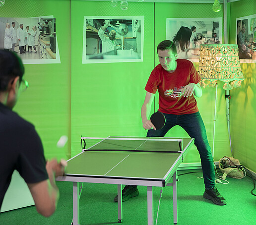 Unter einem Pavillon spielen ein Mitarbeiter und ein Besucher Tischtennis.