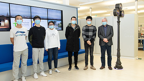 Vier chinesische Studenten und eine chinesische Studentin sowie Professor Worlitz stehen im Laborsaal vor einer Sitzbankreihe.