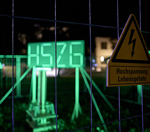 The HSZG logo is illuminated in neon green by fluorescent tubes.