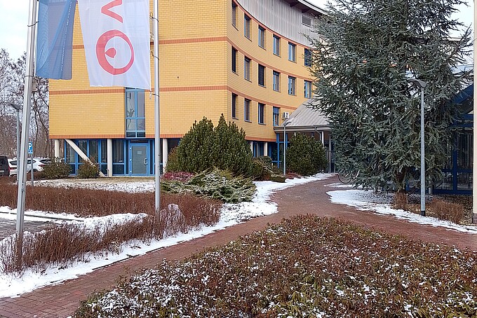 Ein gelbes Gebäude mit Fahnen im Vordergrund auf einem zum Teil mit Schnee bedeckten Platz.