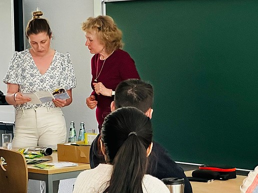 Kristin Groß und eine Studienkollegs-Mitarbeiterin aus Leipzig stehen im Seminarraum vor einer Tafel und sehen sich einen Flyer an.