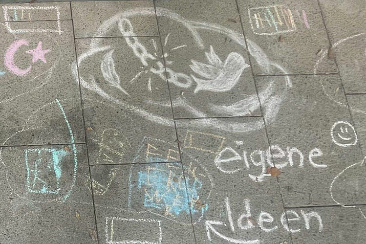 Kreidezeichen auf dem Asphalt mit unterschiedlichen Symbolen wie einer Taube.