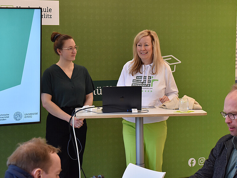 Vice President Prof. Dr. Sophia Keil stands in front of a green press wall at the Introduction to Research Data Management workshop and speaks to the participants.