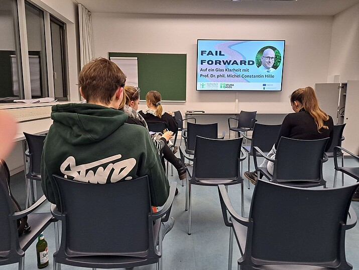 Studierende sitzen in einem Seminarraum auf Stühlen vor einer Präsentation.