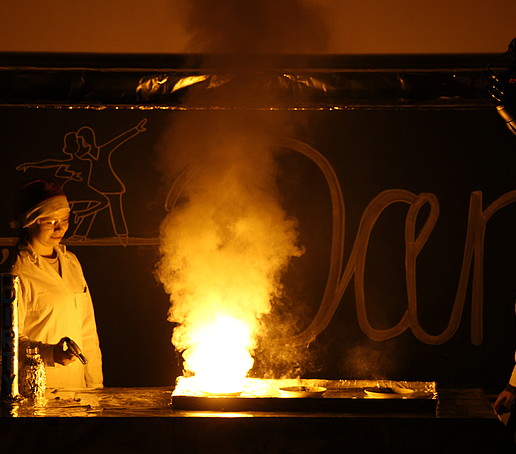 In the dark, two people in Christmas hats conduct a flaming experiment on the podium.