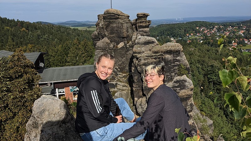 Zwei Studierende sitzen auf einer Steinformation im Zittauer Gebirge und genießen die Aussicht beim Wanderausflug.