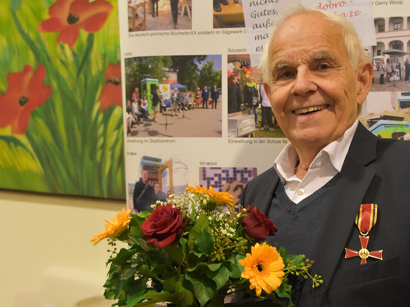 Konrad Kutt wears the Federal Cross of Merit and holds a bouquet of flowers in his hands. He smiles into the camera.