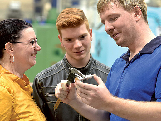 Ein Mann im blauen Poloshirt vermisst einen Gegenstand ein jüngerer Mann und eine Frau schauen dabei zu.