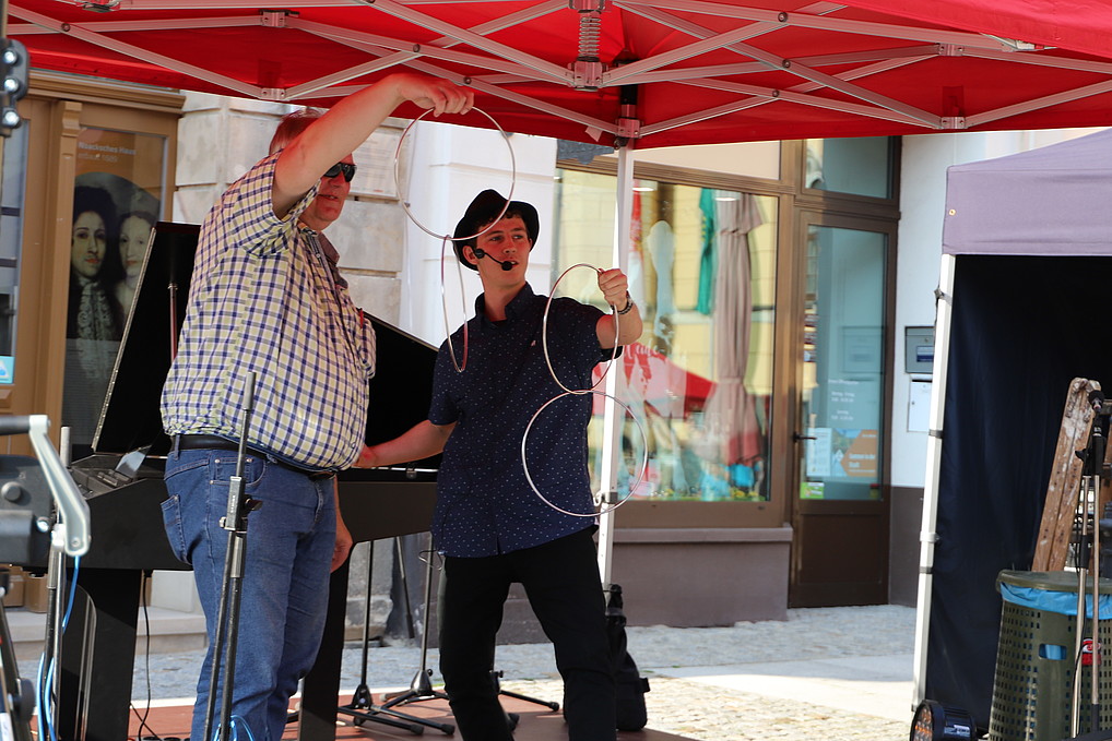 A man and a student stand on a stage with Chinese rings in their hands.