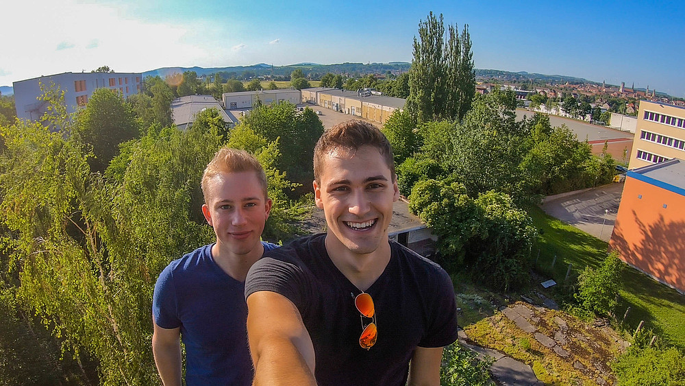Two students take a selfie of themselves above the roofs of the university.