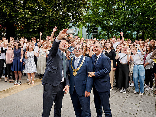A large group of newly enrolled students and the rector stand on the Görlitz campus and laugh into the drone camera.