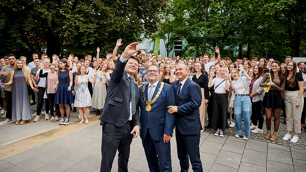 Eine große Gruppe Neuimmatrikulierte und der Rektor stehen auf dem Görlitzer Campus und lachen in die Drohnenkamera.