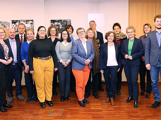 Representatives from the Alliance of Municipal Equal Opportunities Officers in Lusatia, among others, stand for a group photo in a room in front of a wall with black and white pictures and smile into the camera.