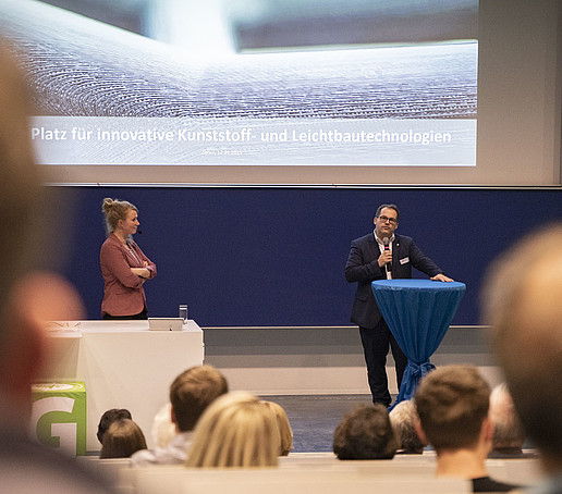 The rector gives a speech in a packed lecture hall. Leonie Liemich stands next to him.