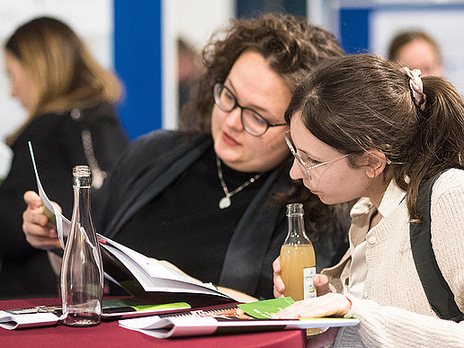 Two visitors study information material at a red bar table