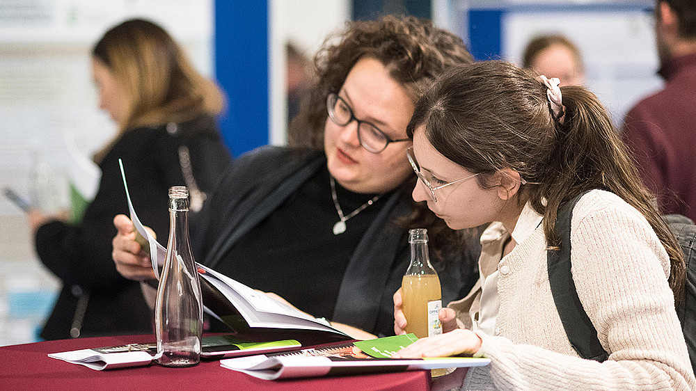Two visitors study information material at a red bar table