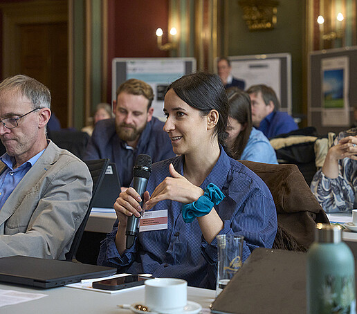 Eine Teilnehmerin sitzt im Publikum und spricht in ein Mikrofon.
