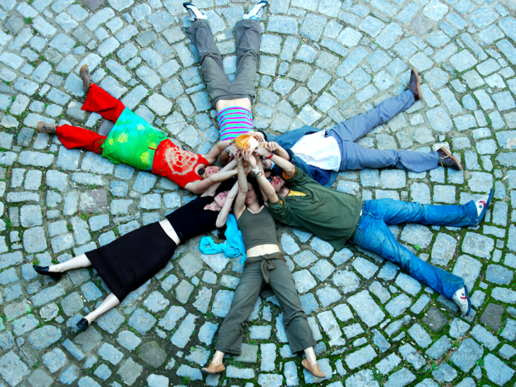 Students lie in a circle on a stone floor and stretch their arms towards a star.