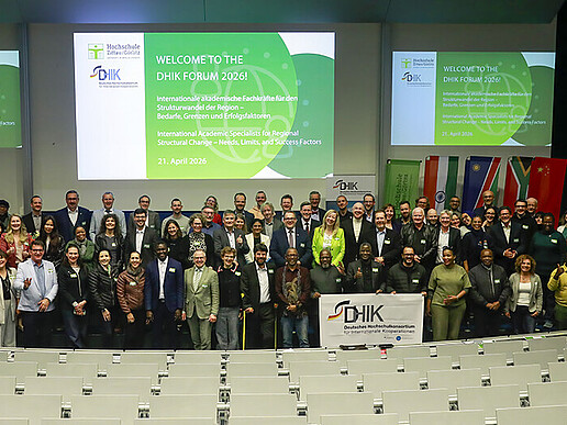 Participants of the forum of the German University Consortium for International Cooperation stand next to each other in front of the rows of seats in the Audimax for a group photo.