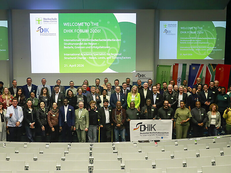 Participants of the forum of the German University Consortium for International Cooperation stand next to each other in front of the rows of seats in the Audimax for a group photo.