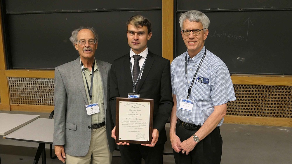 Three men stand next to each other. Dr. Herrmann in the middle holds a certificate in his hands.