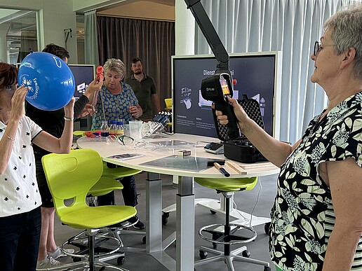 Two teachers test experiments in the School Lab. One is holding a blue balloon in front of her face, the other has a digital measuring device in her hand.