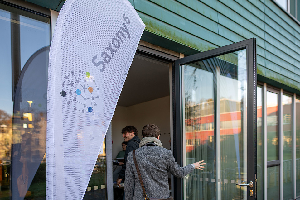 An open door with a beach flag with the Saxony5 logo on it.