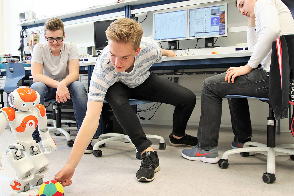 Drei Schüler in einem Labor mit einem Roboter und einem Ball