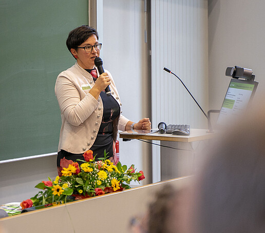 A woman speaks into a microphone in front of a green board in the lecture hall.