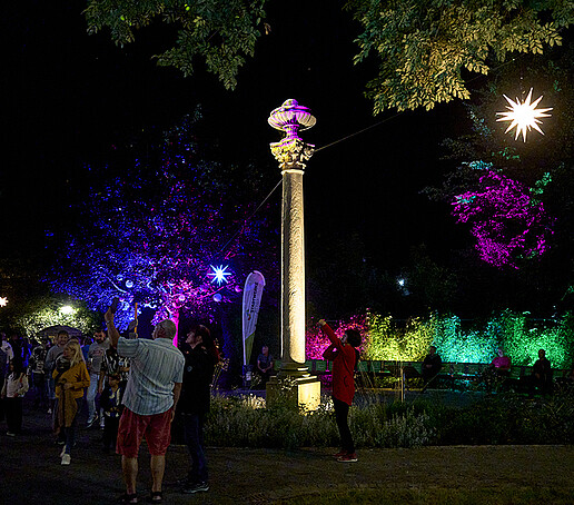 A colorfully illuminated park with visitors.