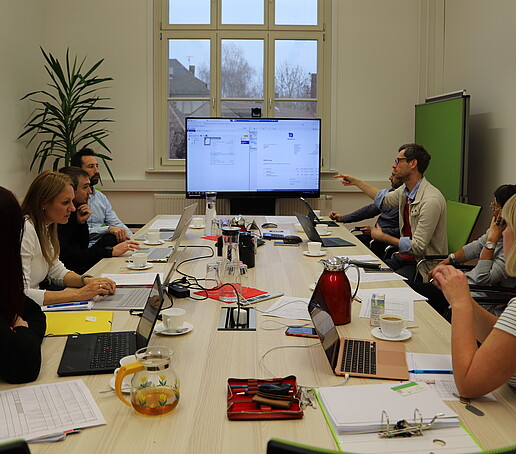 Employees are gathered in a meeting room discussing the topic of DMS with the help of a screen.