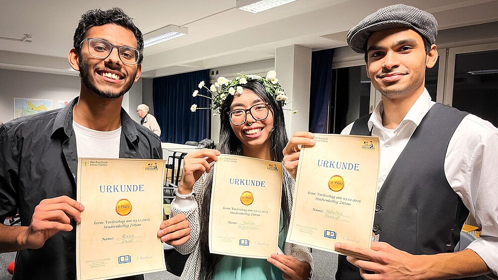 The winner and the two runners-up hold their certificates up to the camera.