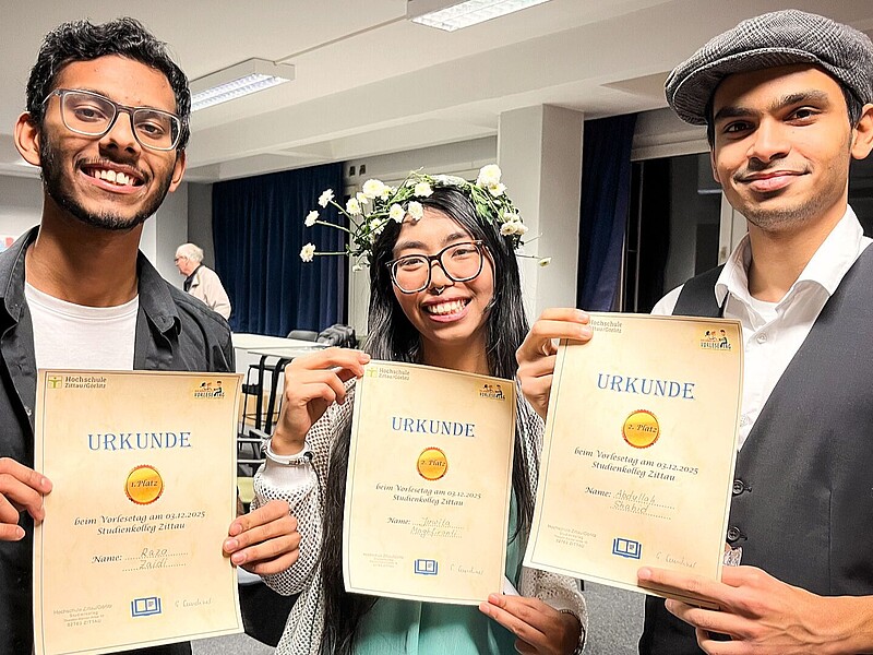 The winner and the two runners-up hold their certificates up to the camera.